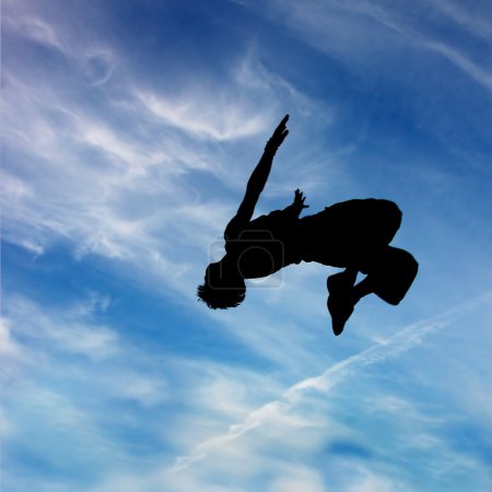 Silhouette of jumping man against blue sky and clouds