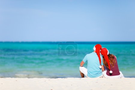 Romantic couple in Santa hats sitting on tropical beach