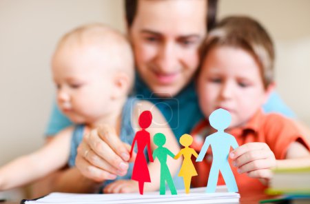 Young father with his two kids holding figures of multicolored paper family
