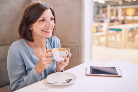 beautiful mature woman smiling while holding her coffee at table