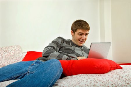 Young casual man working with computer in bed
