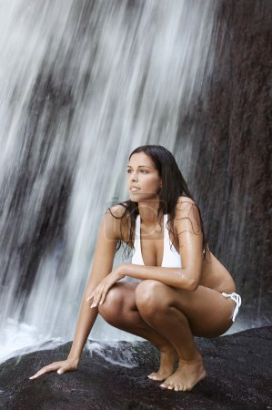 Woman crouching by waterfall