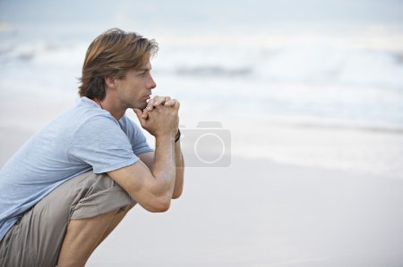 Young man crouching by the sea shore looking at sea
