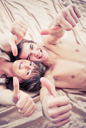 Happy couple lying on bed with thumbs up