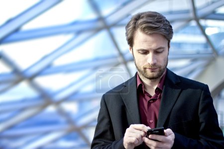 Forty years old businessman standing inside modern office building looking on a mobile phone