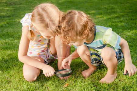 Two little kids playing with magnifying glass outdoors in the d