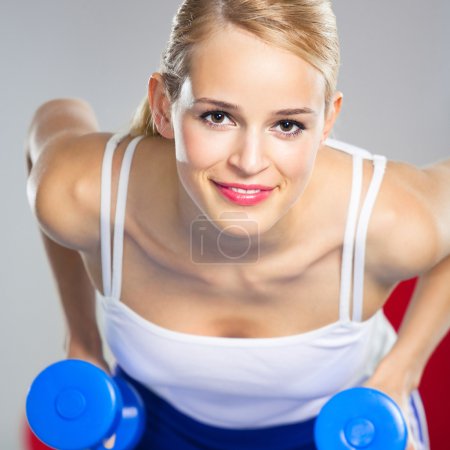 Young happy smiling woman with dumbbells, indoors
