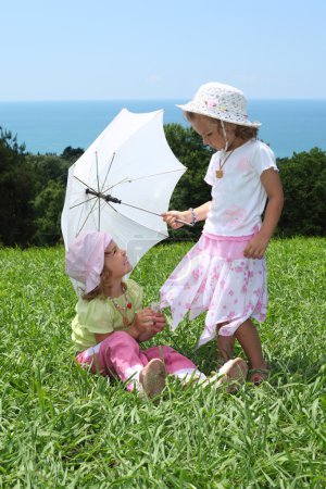 Two little girls with an umbrella on lawn