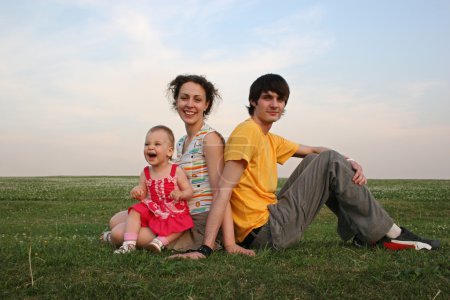 Family with baby sit on evening meadow