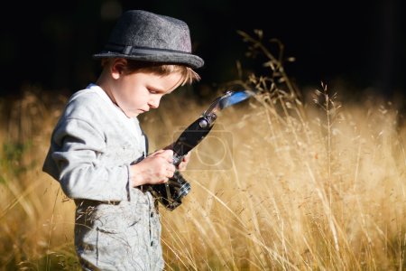 Stylish small boy with retro camera photographing outdoors at sunny autumn day