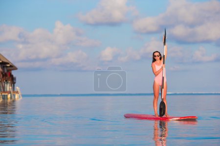 Beautiful young woman surfing on stand up paddle board at exotic vacation