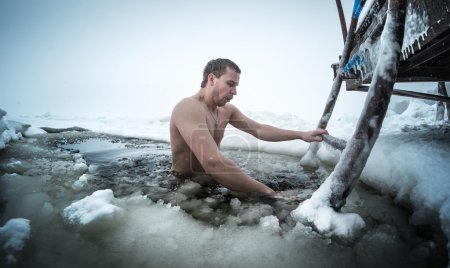 Young man swimming in the ice hole