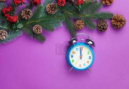 Alarm clock with pine branch on violet background.
