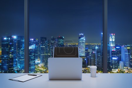 A workplace in a modern panoramic office with New York evening view. A white table, black leather chair. Laptop, writing pad and a cap of coffee are on the table. Office interior. 3D rendering.