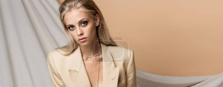 blonde woman in blazer looking at camera on beige draped background, banner