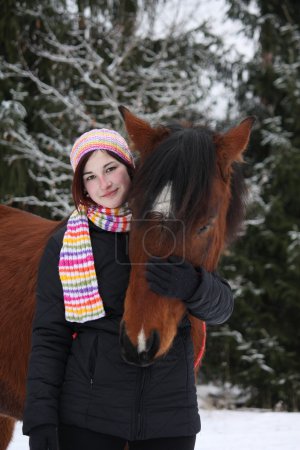 Beautiful teenager girl hugging brown horse in winter