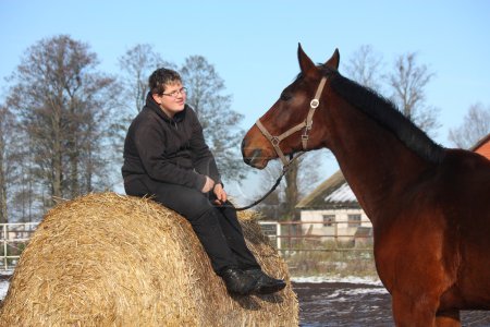 Teenager boy resting on the hay bale and bay horse