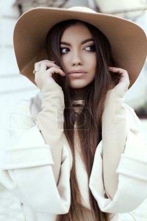 glamour girl with dark straight hair wears luxurious beige coat with elegant hat 