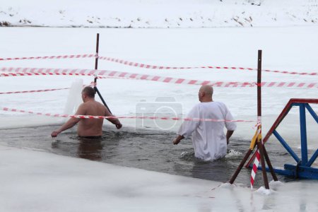 Winter baptism rite, a two Russian people man in a white shirt swimm in the ice hole water on a frosty winter day, epiphany bathing christianity tradition