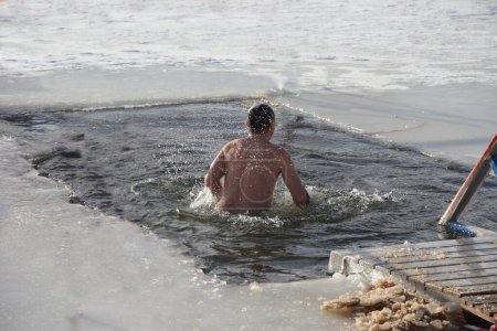 Winter baptism rite, a Russian man in a white shirt swimm stand on wooden pathway near the ice hole water on a frosty winter day, epiphany bathing christianity tradition