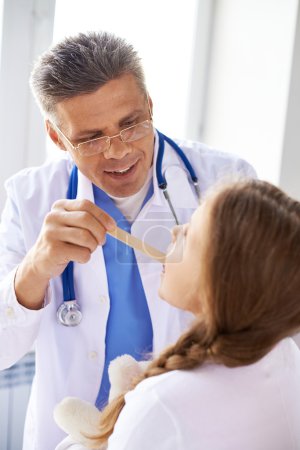 Doctor checking up throat of girl