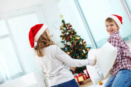 Children in Santa caps fighting with pillows