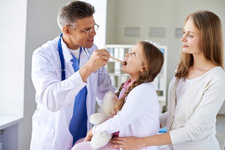Doctor checking up throat of girl