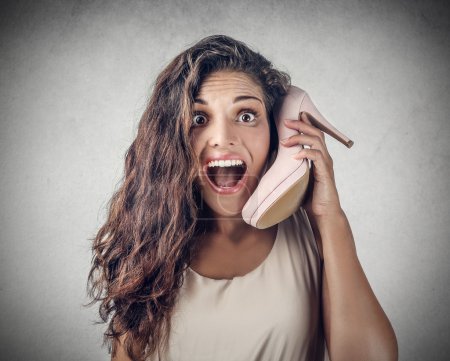 Young surprised girl using a shoe instead of a mobile phone