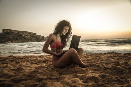 Beautiful girl using a pc at the beach at sunset