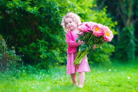 Little girl with peony flowers in the garden