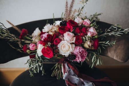 Wedding. Boutonniere. Grain. Artwork. A bouquet of red flowers, pink flowers and greenery with silk ribbons is in the black chair