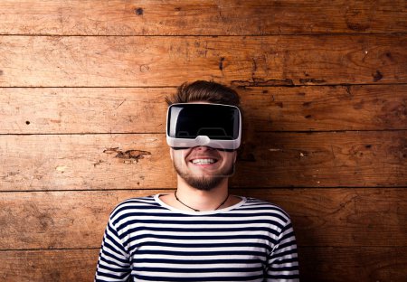 Man wearing virtual reality goggles. Studio shot, wooden background