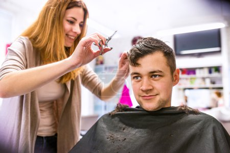 hairdresser cutting hair of young client.