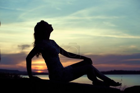Silhouette of the young woman sitting close to the sea