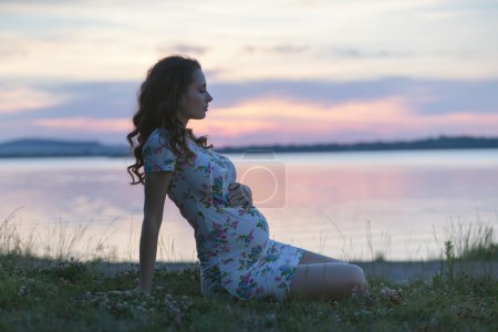 Calm pregnant woman sitting on the lakeside
