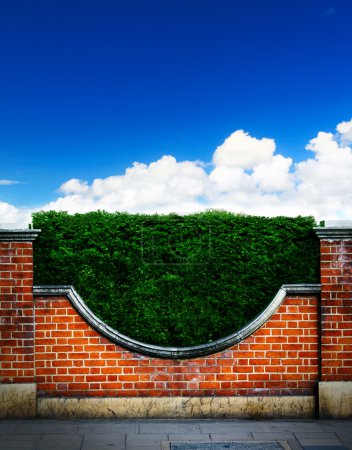Art shrubs and brick fence on blue sky background