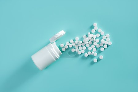 Bottle with white pills coming out over green background