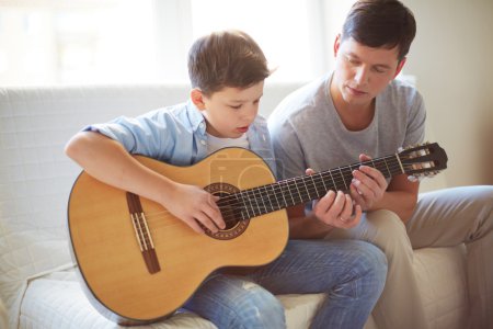 Man teaching his son how to play guitar