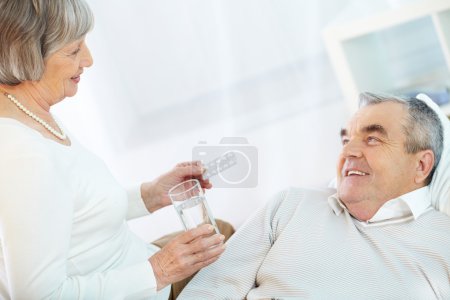 Senior woman offering pill to sick husband