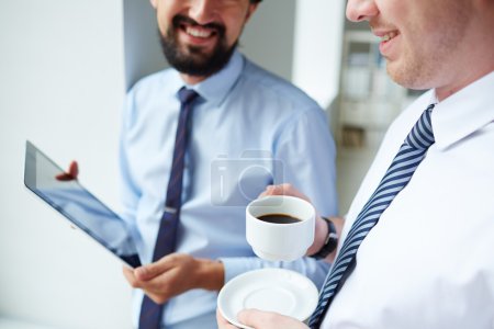 Businessman holding cup and listening tocolleague