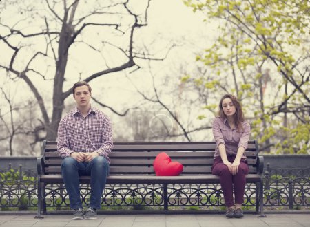 Sad teens sitting at the bench at the park