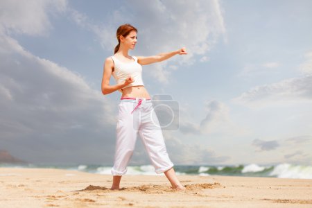 athletic woman performing a kick in an sand beach