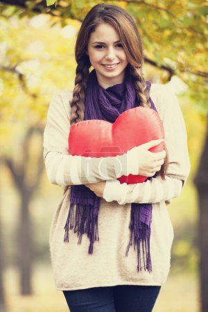 Redhead girl with toy heart at autumn park.