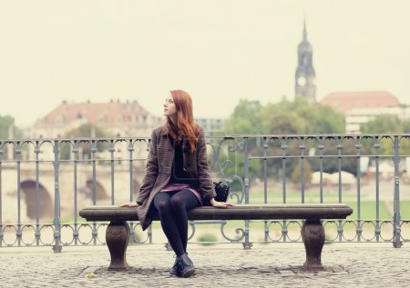 Redhead girl sitting on the bench near river in Dresden.