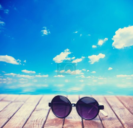 Sunglasses on wooden table and the sea on background.