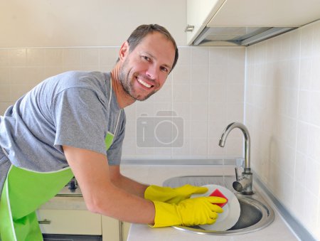 Smiling man washing dish in the kitchen