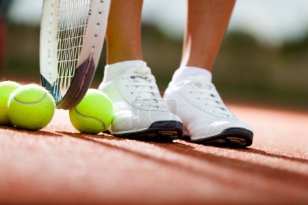 Legs of athlete near the tennis racket and balls