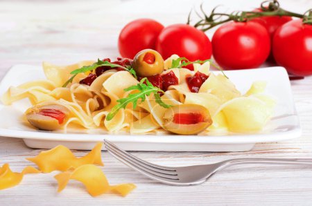 Pasta with tomato and arugula on the wooden table