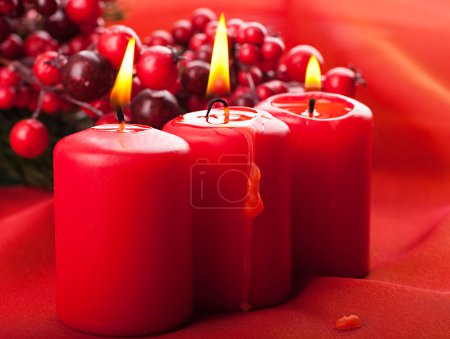 Christmas card. branch of a fur-tree and a candle on a red background