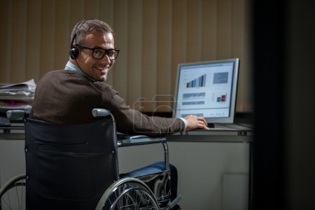 Man on wheelchair is working late in the office